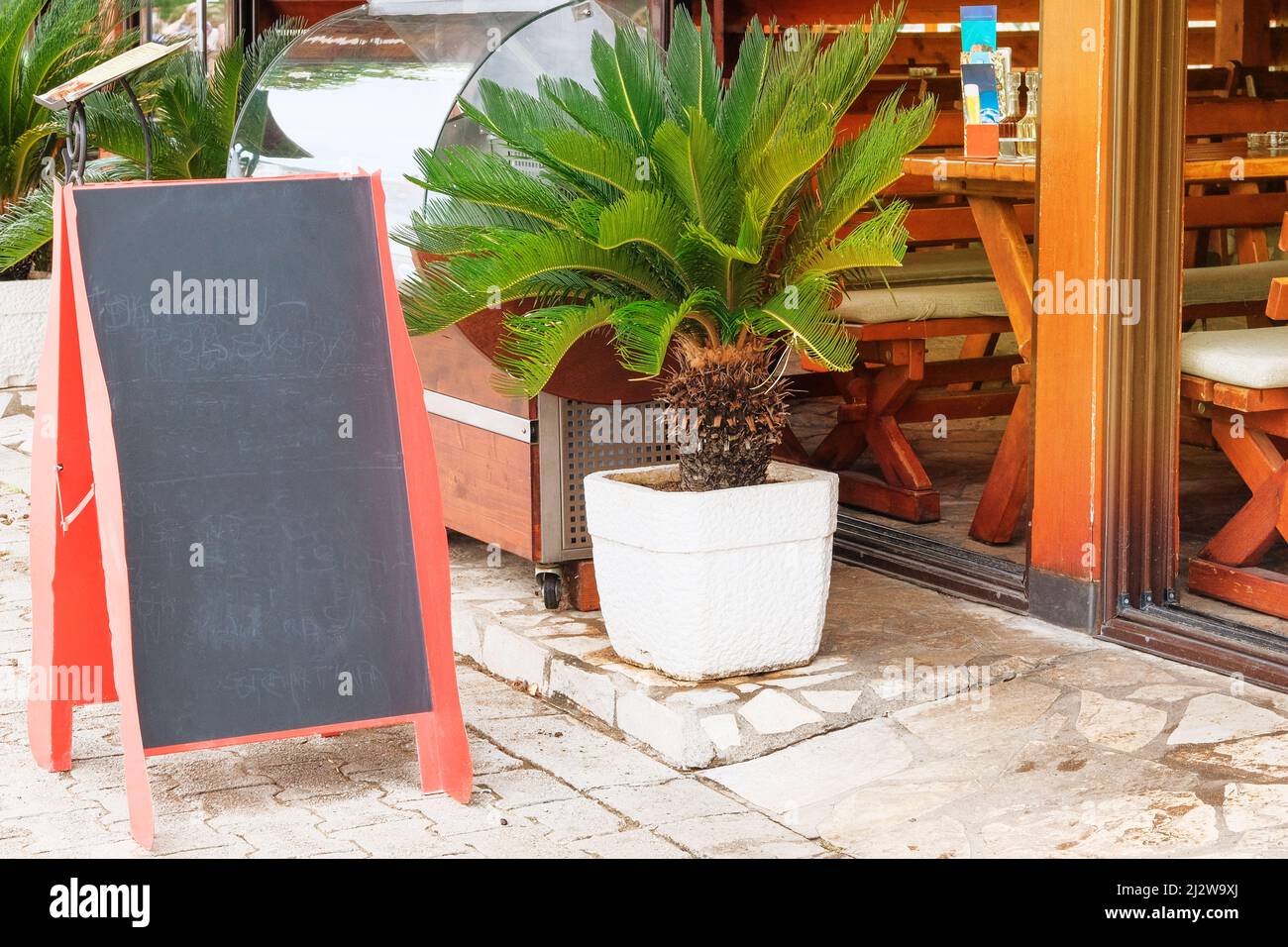 Schwarzes Tafelmenü in Farbe für Text, Nachricht oder Werbung. Mockup steht in der Nähe des Restaurants an der Küste. Sonniger Tag. Stockfoto