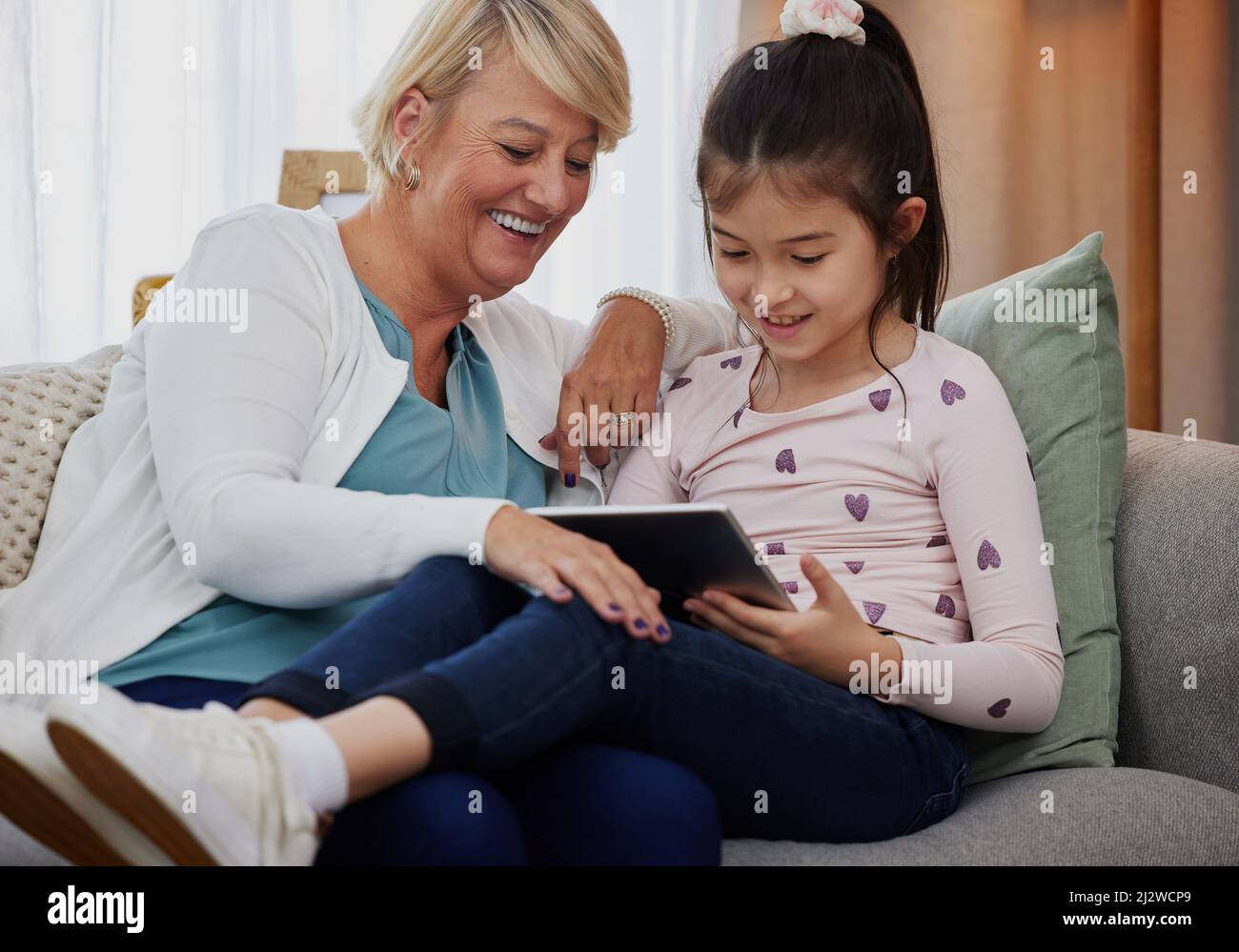 Lassen Sie mich Ihre Punktzahl sehen Aufnahme eines entzückenden kleinen Mädchens, das ein digitales Tablet benutzt, während es zu Hause mit ihrer Großmutter sitzt. Stockfoto