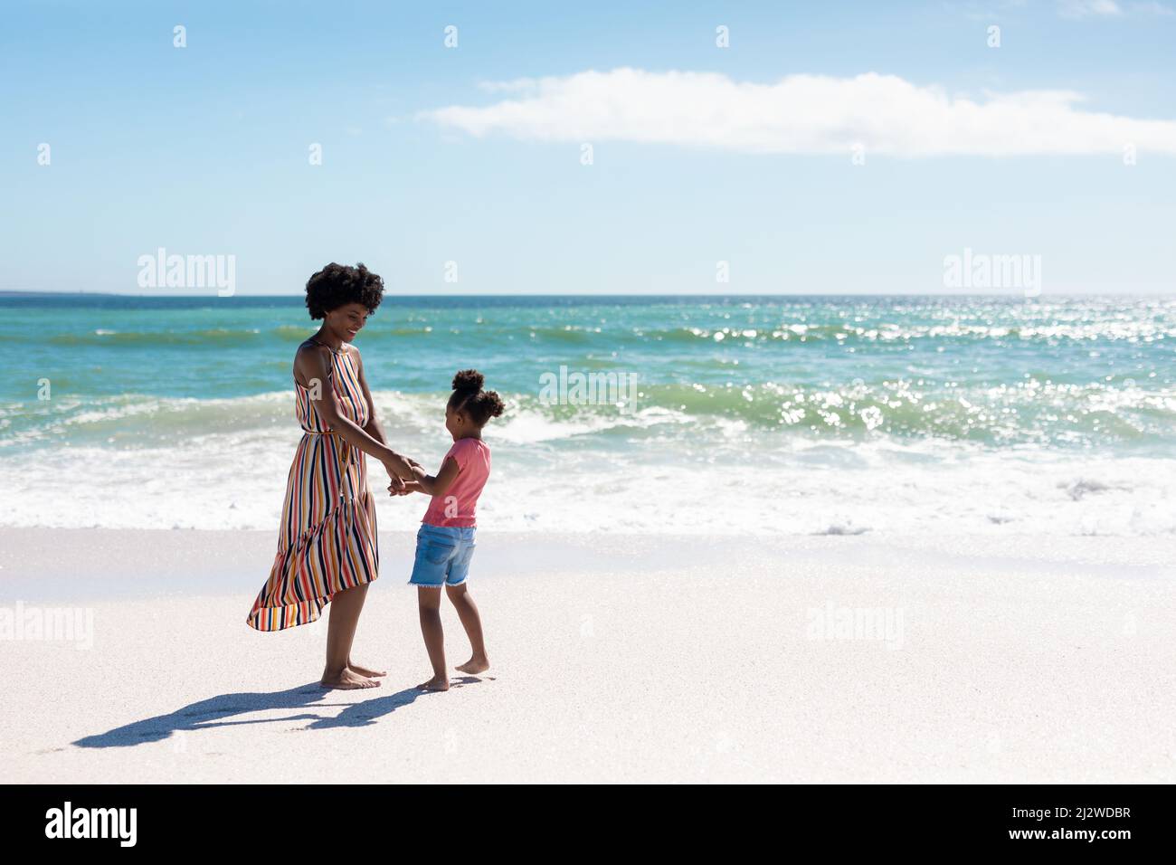 Die ganze Länge der glücklichen afroamerikanischen Mutter und Tochter, die am sonnigen Tag am Strand spielen Stockfoto