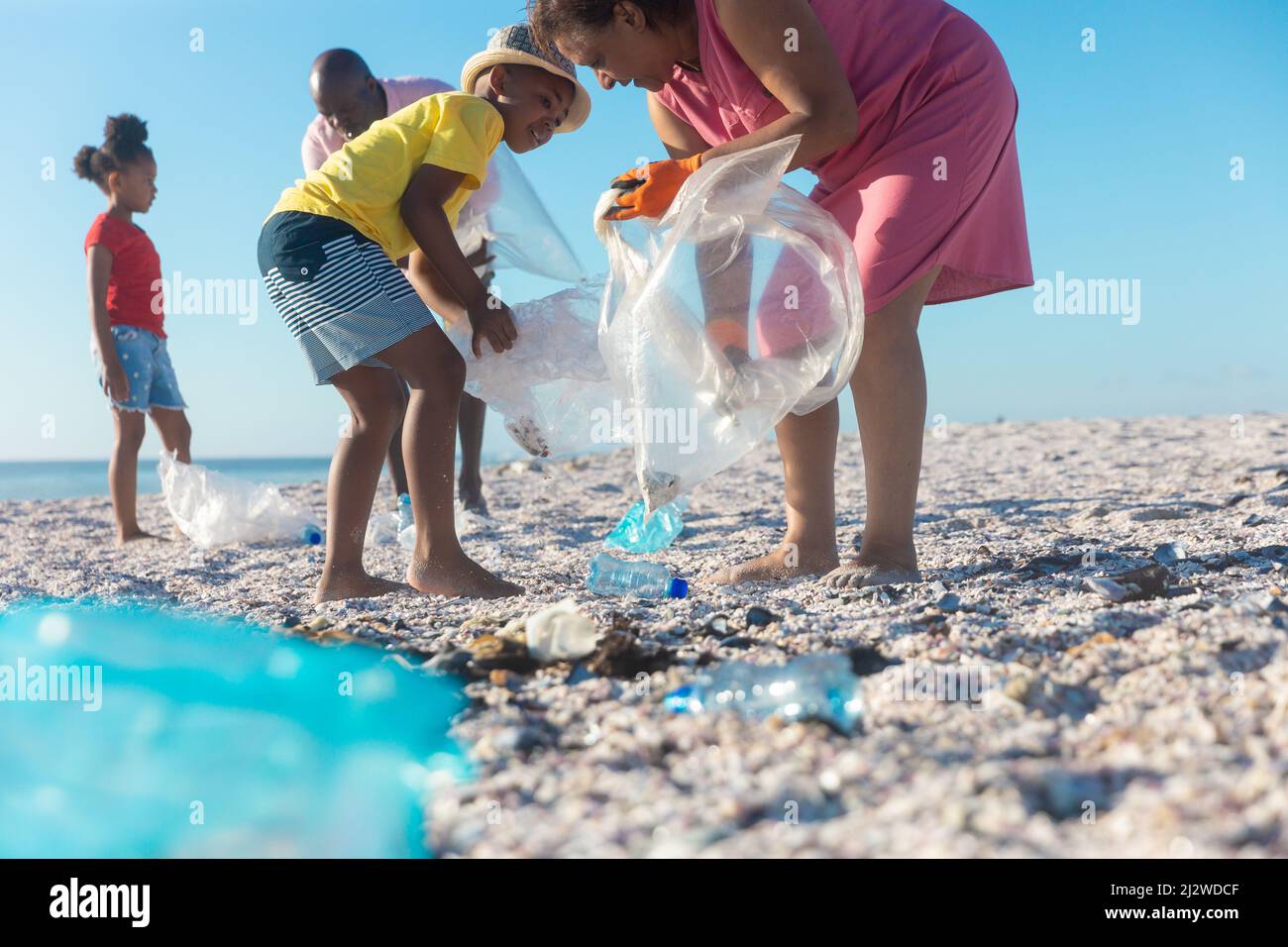 afroamerikanische Großeltern und Enkelkinder sammeln Plastikmüll am Strand an sonnigen Tagen Stockfoto