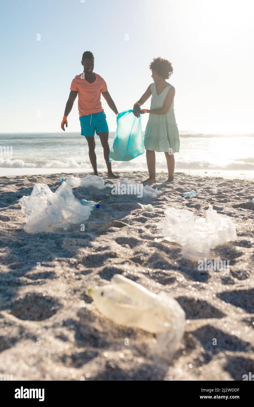 Oberflächennahe Ansicht von Müll auf Sand mit afroamerikanischem Paar, das Abfall am Strand sammelt Stockfoto
