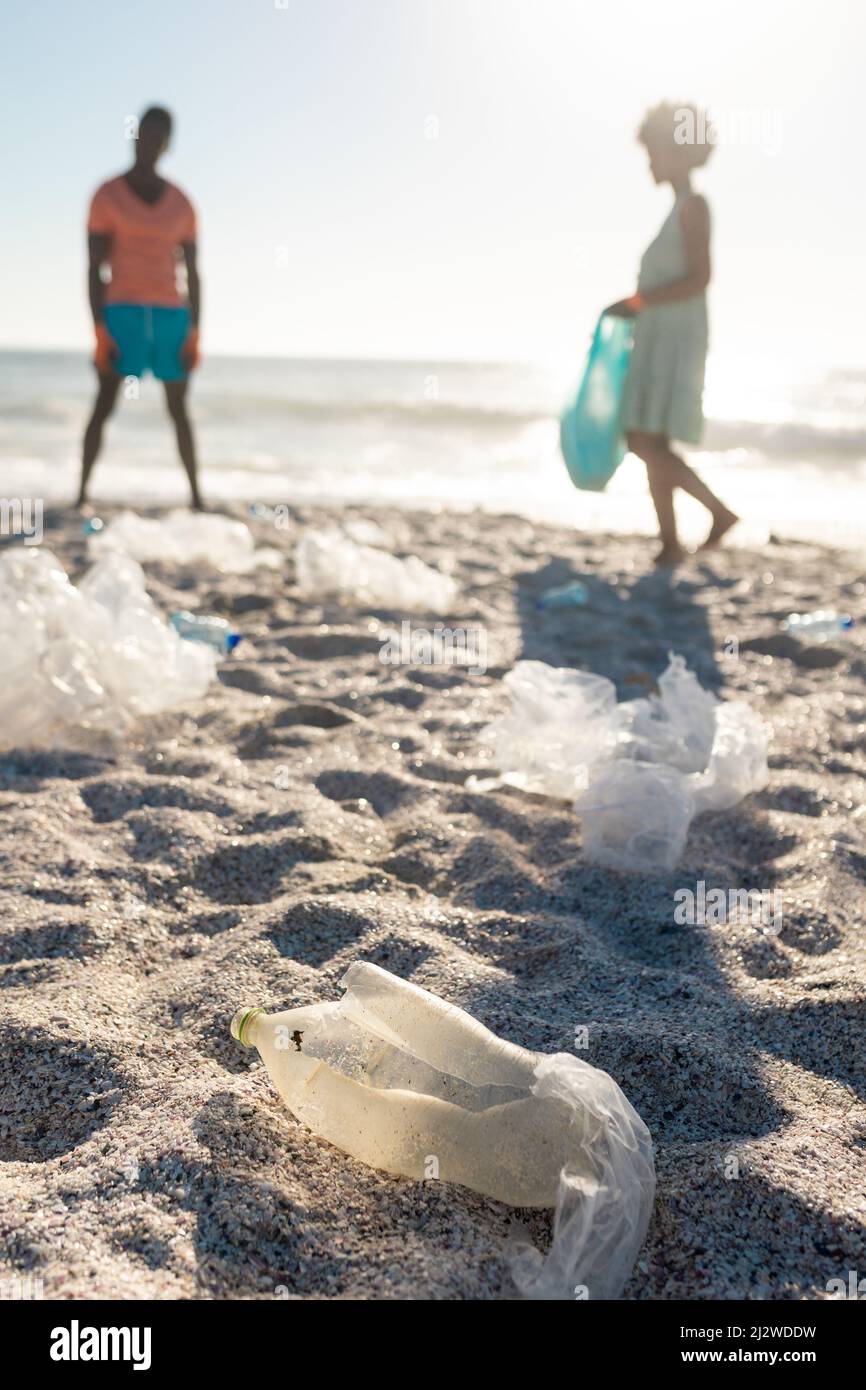 Oberflächennahe Ansicht des Plastikmülls, der gegen den afroamerikanischen Strand des Paares verstreut ist Stockfoto