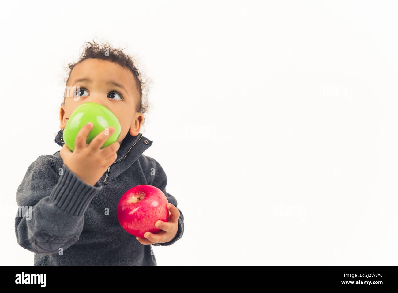 Kleiner afroamerikanischer gewellter Junge, der nach oben schaute und große grüne und rote Äpfel hielt, Studio schoss weißen Hintergrund mittlerer Nahaufnahme Kopierraum. Hochwertige Fotos Stockfoto