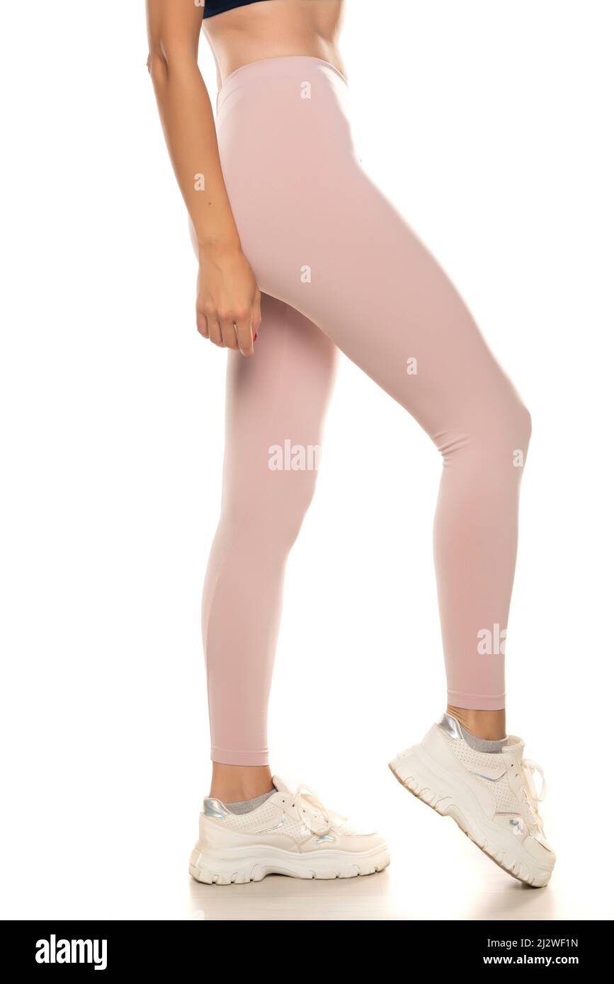 Seitenansicht einer weiblichen Beine in einer rosa Sportstrumpfhose und Sneakers auf weißem Hintergrund. Stockfoto