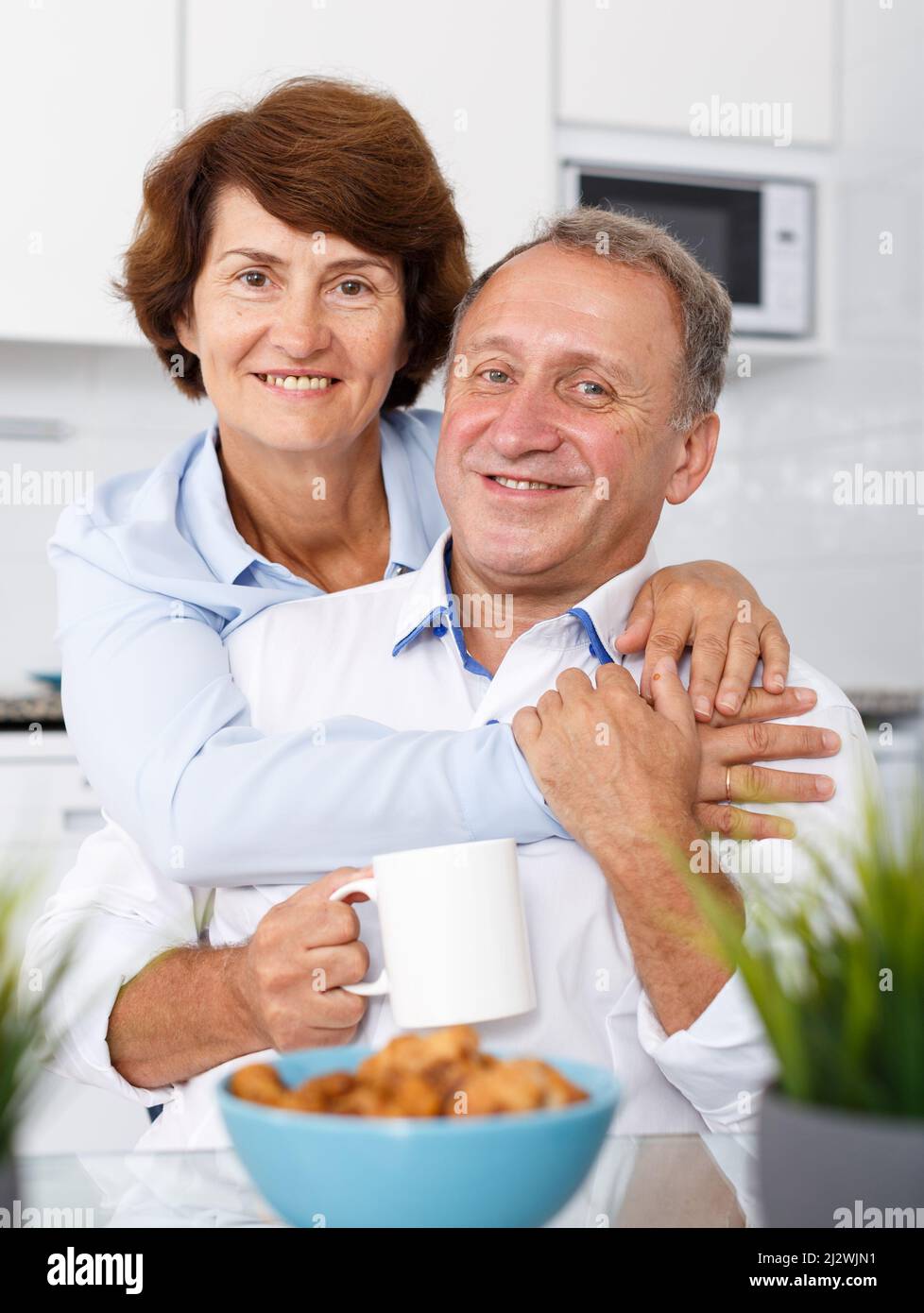 Reifes Familienpaar umarmt am Küchentisch während des Teetrinkens Stockfoto