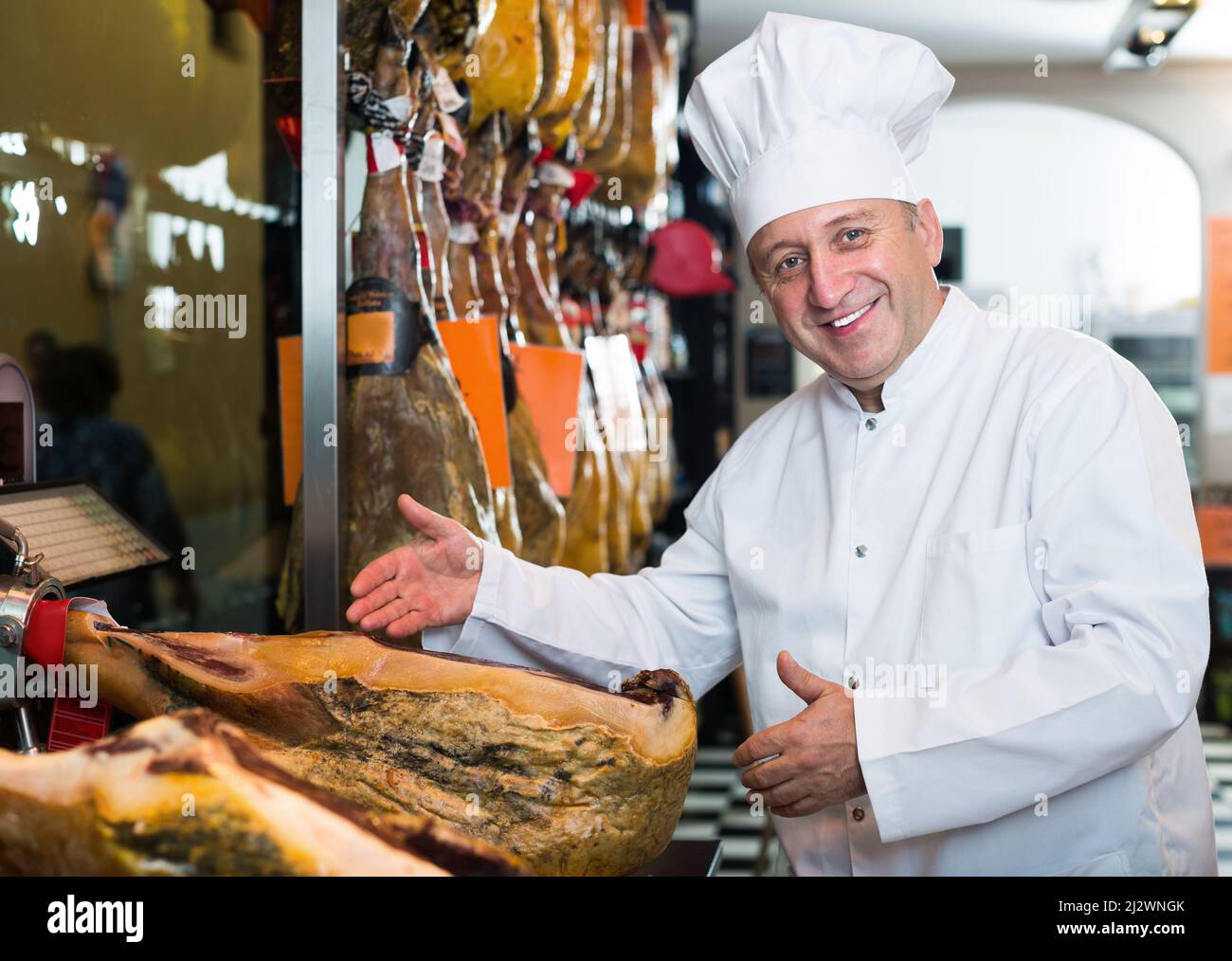 Ein älterer Verkäufer, der spanischen Jamon zeigt Stockfoto