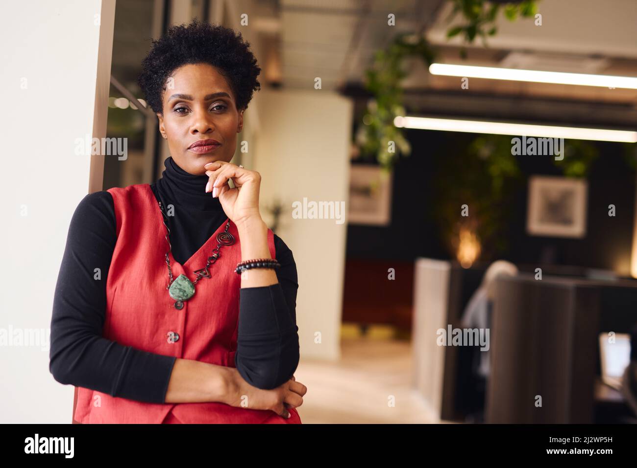 Porträt einer reifen schwarzen Frau mit der Hand auf dem Kinn, die mit einem nachdenklichen Ausdruck im Coworking Space auf die Kamera blickt Stockfoto