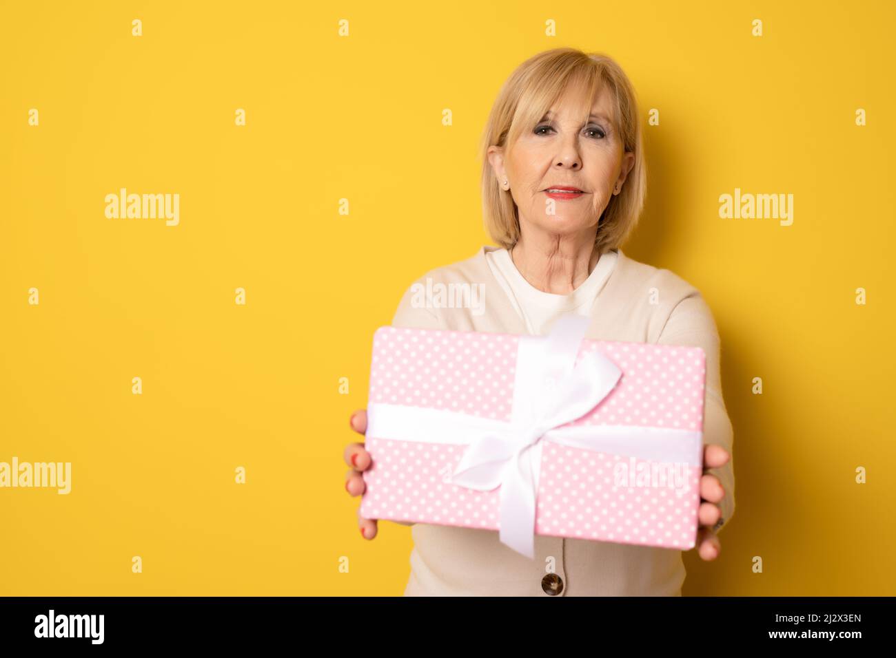 Portrait von fröhlich positiv froh charmant im Alter Frau hält Geschenkbox in rosa Paket stehend isoliert über gelben Hintergrund. Stockfoto