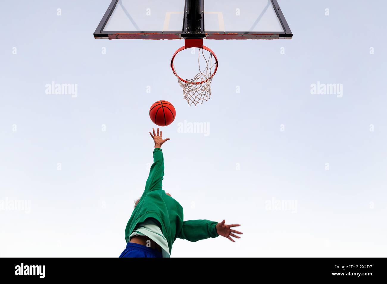 Nicht erkennbare lateinerin, die in einem Basketballkorb von unten mit dem Himmel im Hintergrund schießt, Konzept des urbanen Sports im Freien, Kopierraum f Stockfoto