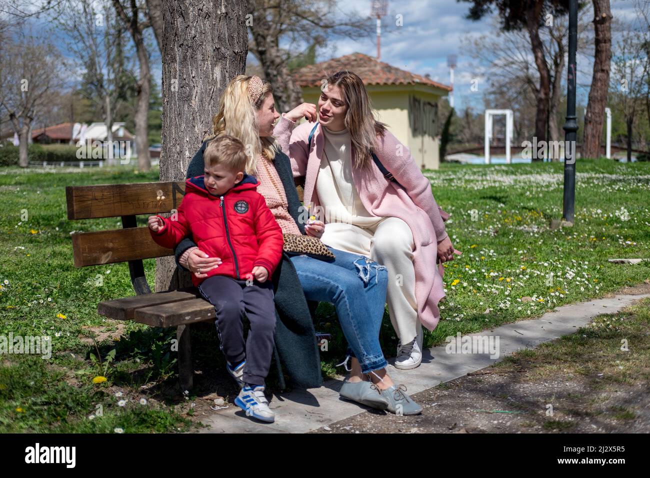 Mutter mit Sohn und Freundin sitzen an einem sonnigen, warmen Tag auf einer Bank im Park Stockfoto