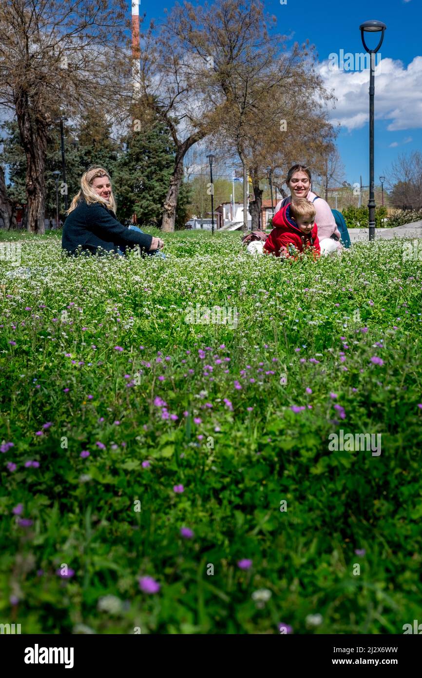 Mutter mit Sohn und Freundin sitzen an einem sonnigen, warmen Tag auf dem Rasen im Park Stockfoto