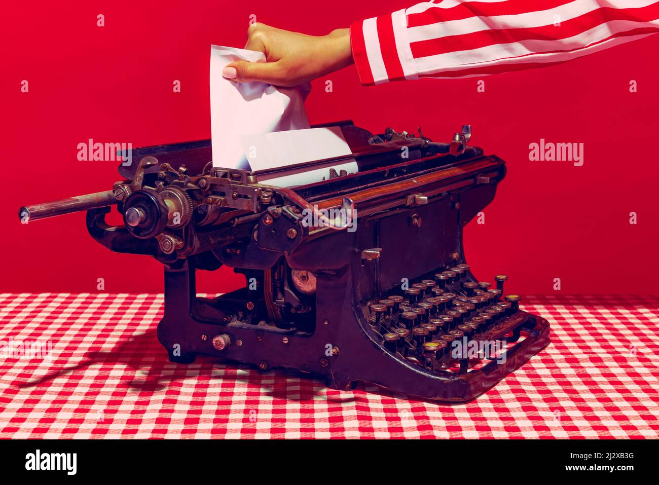 Pop-Art-Fotografie. Weibliche Hand mit Retro-Schreibmaschine isoliert auf hellrotem Hintergrund. Vintage-Retro-Style. Stockfoto