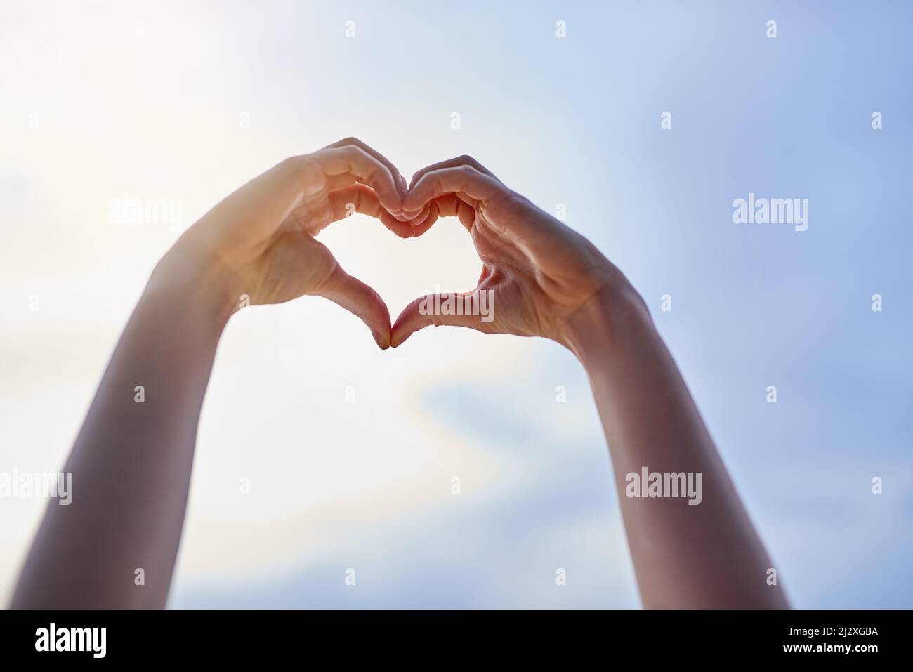 Ich liebe den Sommer. Abgeschnittene Handaufnahmen, die eine Herzform gegen einen blauen Himmel bilden. Stockfoto