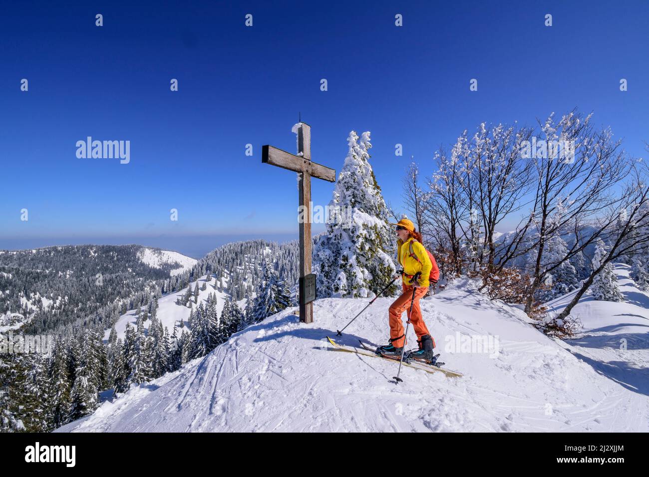 Frau auf Skitour steht am Gipfelkreuz des Predigtstuhls, Predigtstuhls, Chiemgauer Alpen, Oberbayern, Bayern, Deutschland Stockfoto