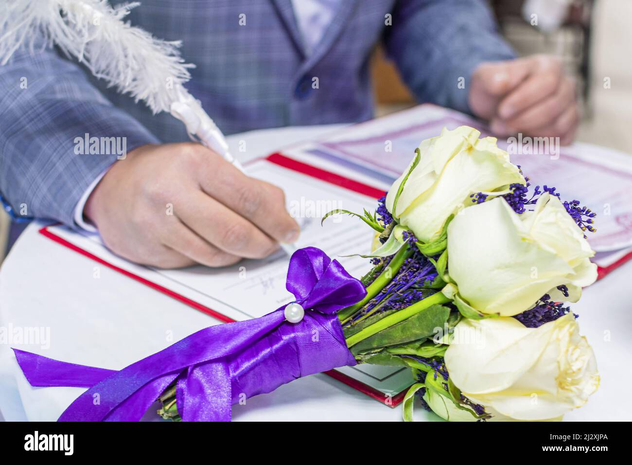 Hand des jungen Mannes, Bräutigam, unterzeichnet Ehedokument mit schönen Stift. Vor ihm liegt der Brautstrauß. Stockfoto