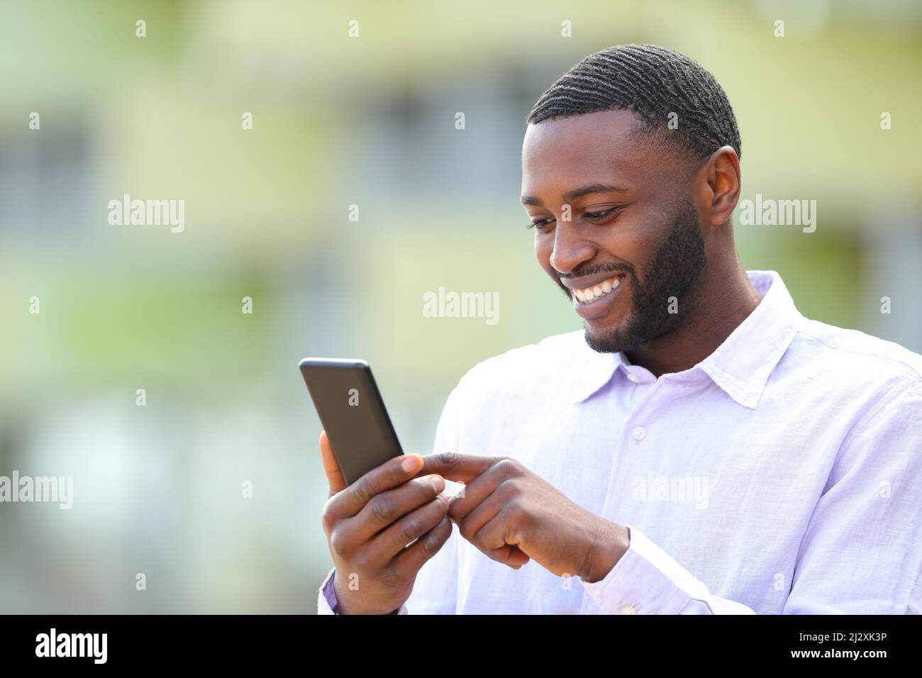 Glücklicher Mann mit schwarzer Haut, der mit dem Smartphone nach draußen geht Stockfoto