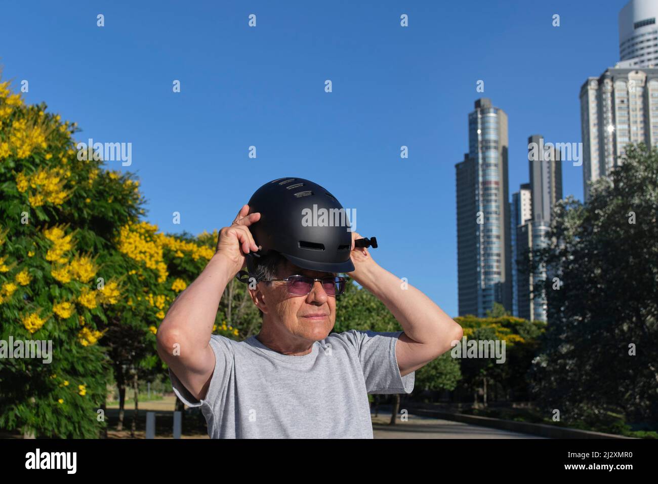 Ein älterer hispanischer Mann, der in einem Stadtpark einen Sporthelm aufsetzt. Konzepte des aktiven städtischen Lebens, des Wohlfühlens und der Verkehrssicherheit. Stockfoto