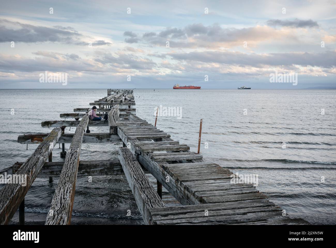 Junger Mann, der auf dem Steg in Playa Norte, Punta Arenas, Patagonien, Chile, Südamerika sitzt Stockfoto