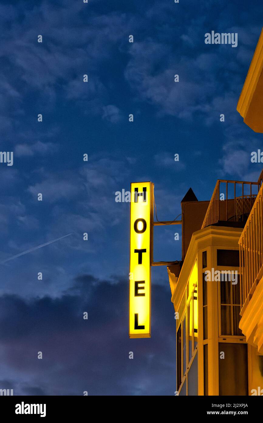 Ein hell erleuchtetes Hotelschild zeigt sich deutlich vor dem dunklen Himmel dahinter. Das Schild ist senkrecht und an der Vorderseite des Hotels angebracht. Stockfoto