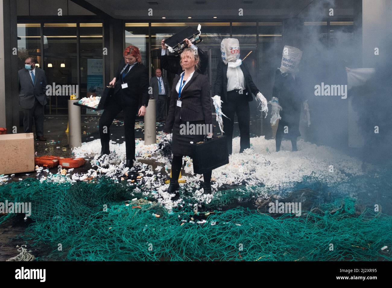 London, Großbritannien. 4. April 2022. Mitglieder der Ocean Rebellion, führen kreative Theateraktionen im Londoner Hauptquartier der Internationalen Seeschifffahrtsorganisation (IMO) durch am Morgen des 1. Tages der IMO-Konferenz zur Vermeidung und Reaktion auf Umweltverschmutzung, verschütteten geeignete Mitglieder der Ocean Rebellion gefälschte ‘Nurdles', Und Öl unter den weggeworfenen Fischabfällen und schwarzen Kohlenstoff- und Plastiktüten, während ein Paar schmutzige Reinigungskräfte versuchen, die Beweise mit ihren Greenwash-Diensten zu verbergen. Quelle: Joao Daniel Pereira/Alamy Live News Stockfoto