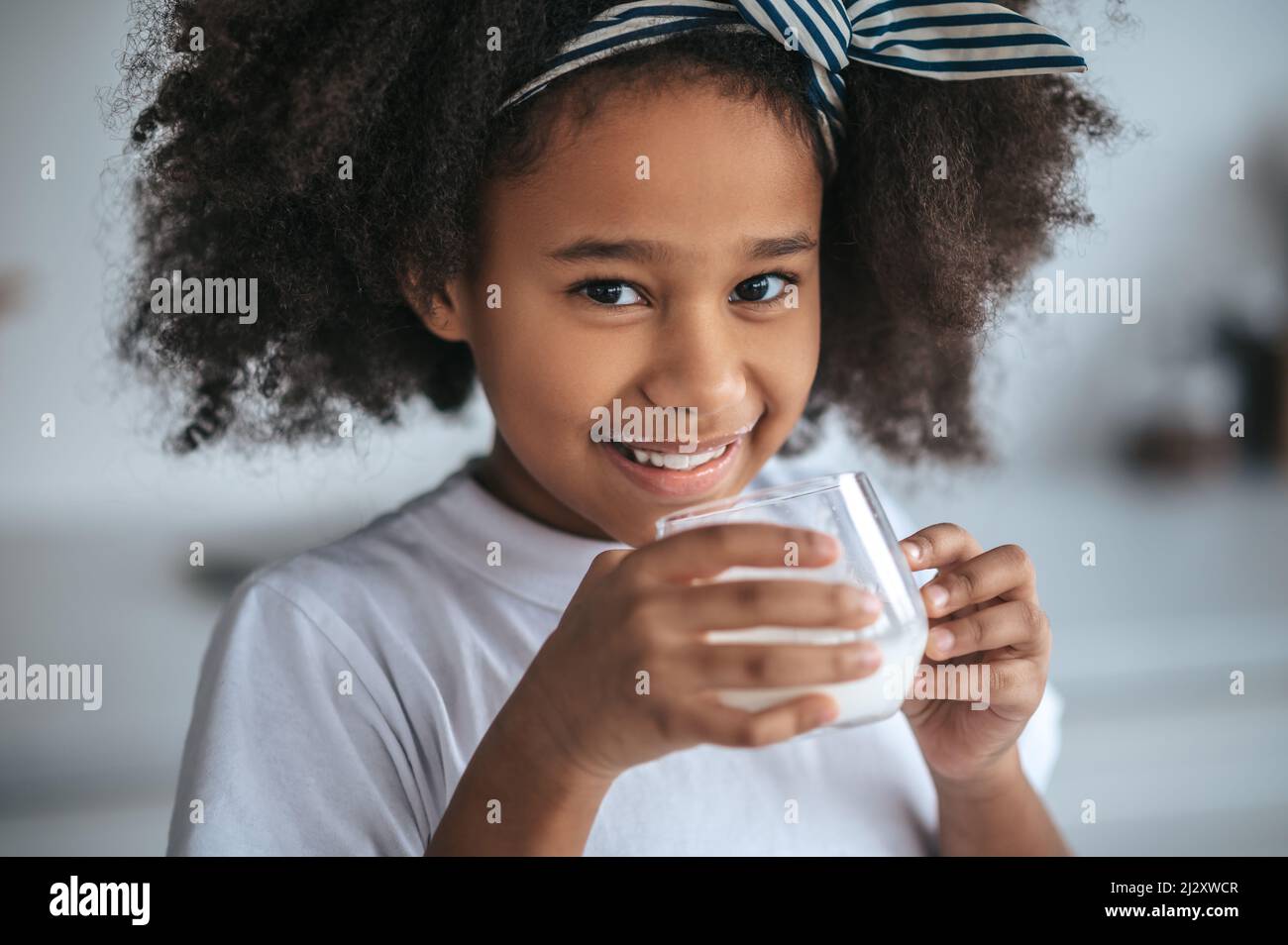 Nettes dunkelhäutig Mädchen mit einem Glas Milch Stockfoto