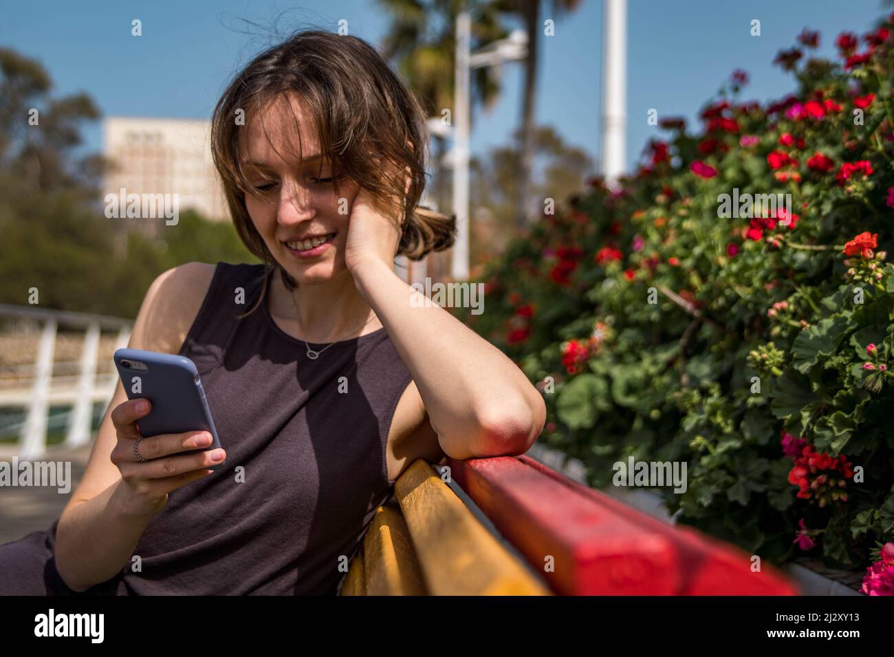 Bild der 30-jährigen Frau mit Halterungen Zahnspangen Gerät mit ihrem Mobiltelefon im Freien auf einer Bank sitzen Stockfoto