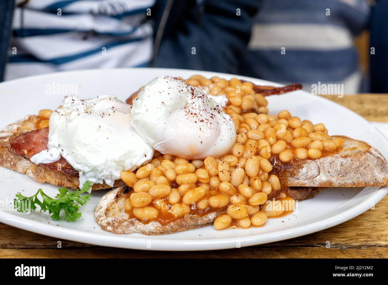 Ein gesünderes traditionelles englisches Frühstück mit Bohnen auf Toast. Es wird mit saurem Teigbrot serviert und die Eier werden pochiert und nicht gebraten Stockfoto