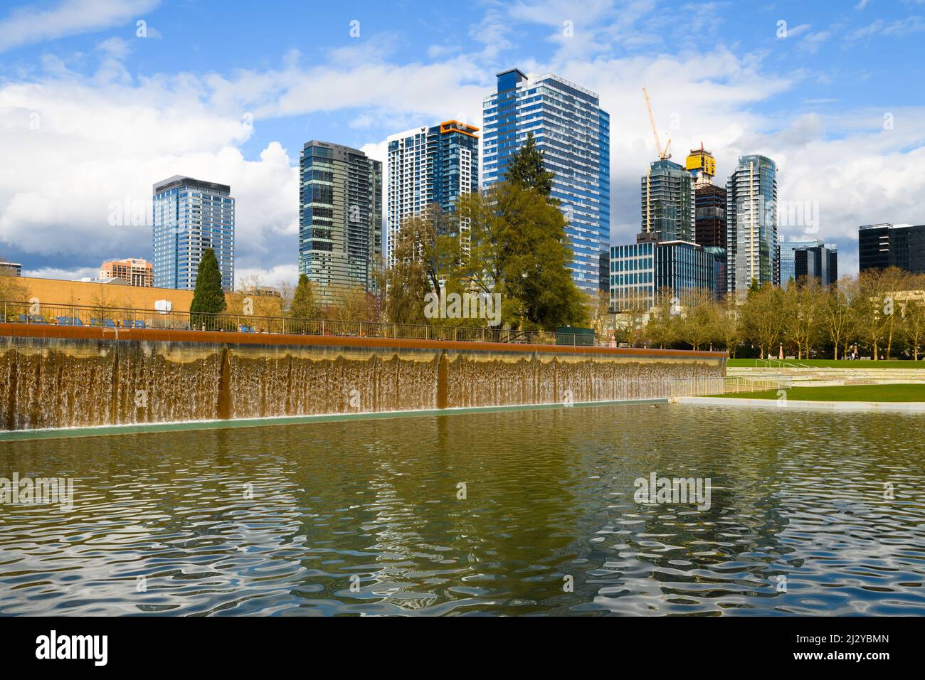 Bellevue, WA, USA - 31. März 2022; Wasserfall im Downtown Park in Bellevue vor der modernen Skyline der Stadt und geschwollenen Wolken im Frühling Stockfoto