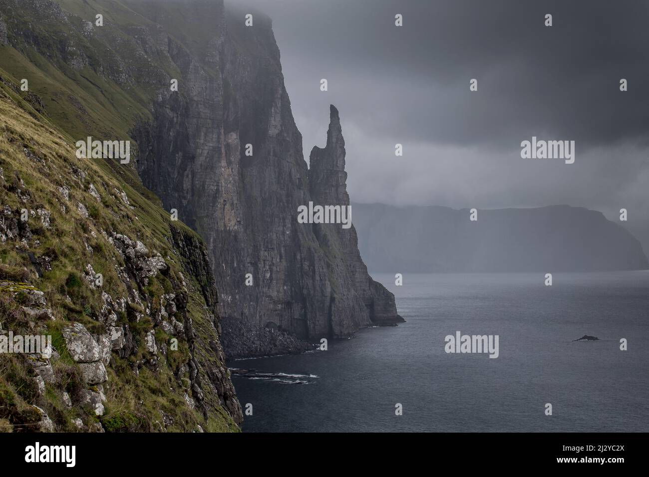 Blick entlang der Klippen zu Witches Finger, Meer Stapel. Vagar, Färöer. Dunkle Regenwolken. Stockfoto