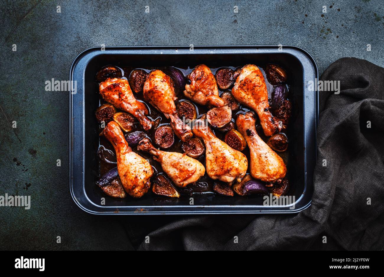 Gebackene Hähnchenbeine, Drumsticks mit süßen Feigen und Zwiebeln in balsamischer Marinade auf schwarzem Backblech, rostiger grüner Tischhintergrund, Draufsicht Stockfoto