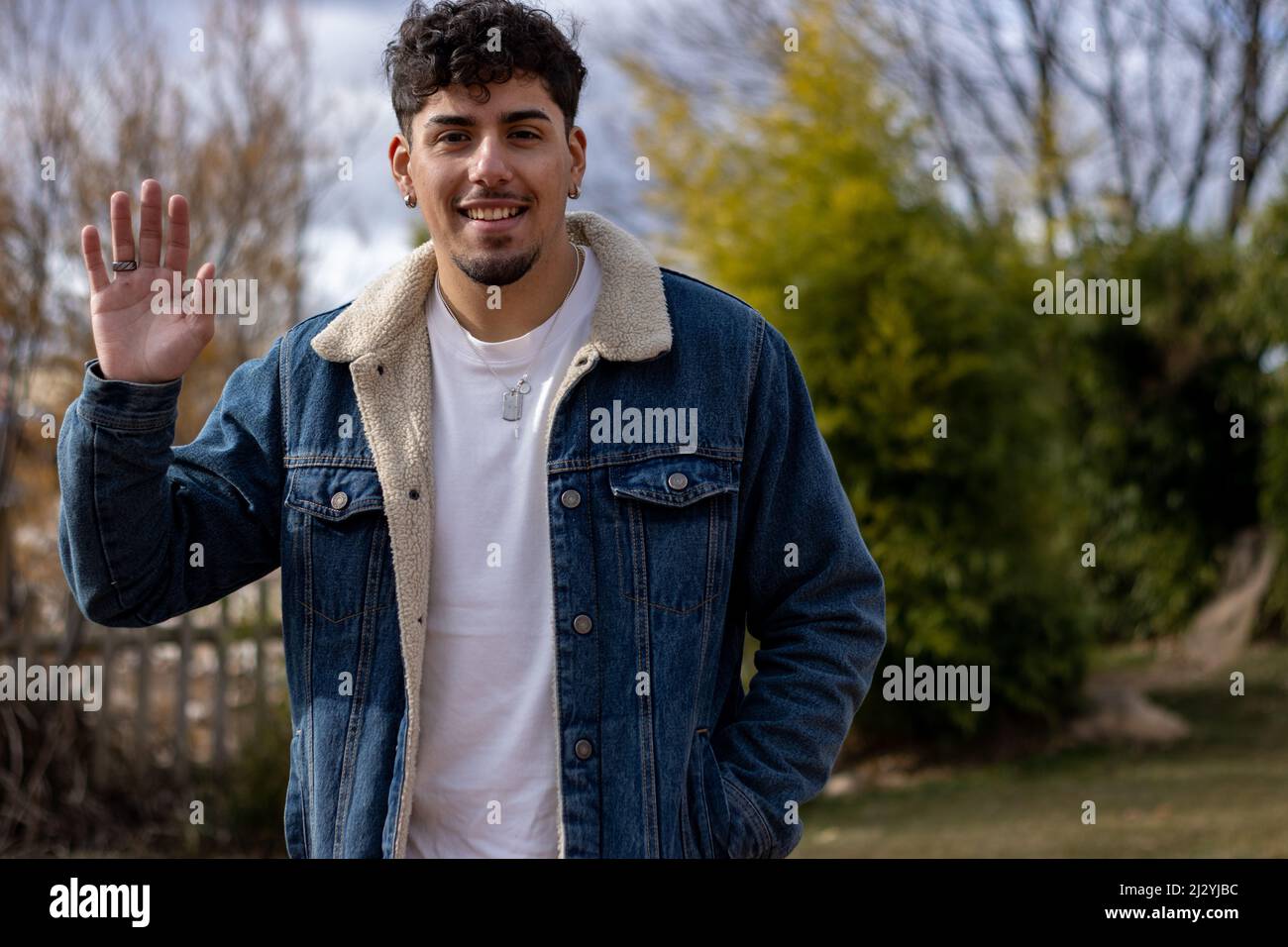 Ein hispanischer junger Mann winkt und lächelt vor der Kamera Stockfoto