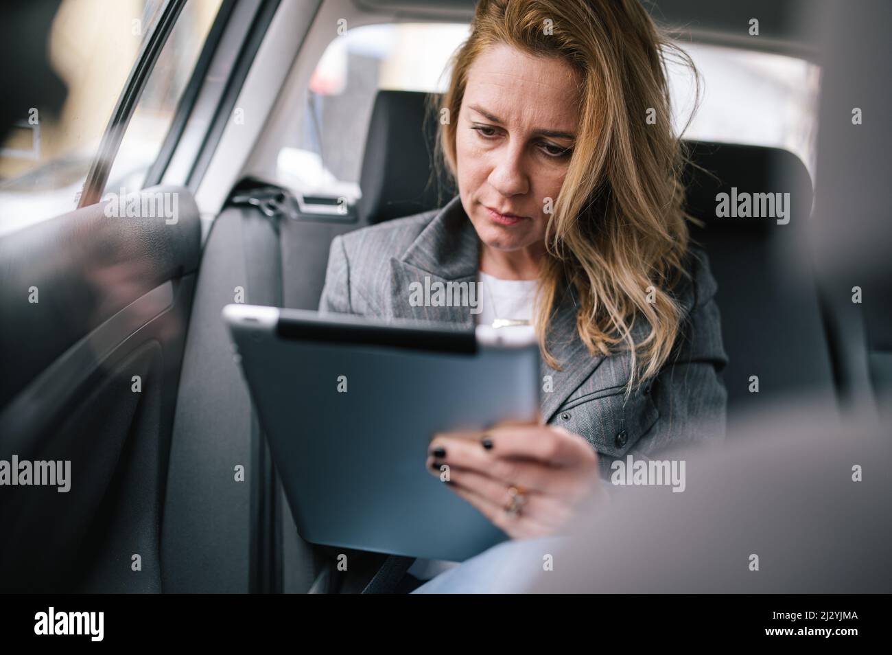 Eine junge Geschäftsfrau sitzt auf dem Rücksitz eines Autos und nutzt überlegt ein Tablet, um ihren Arbeitszeitplan zu organisieren. Stockfoto