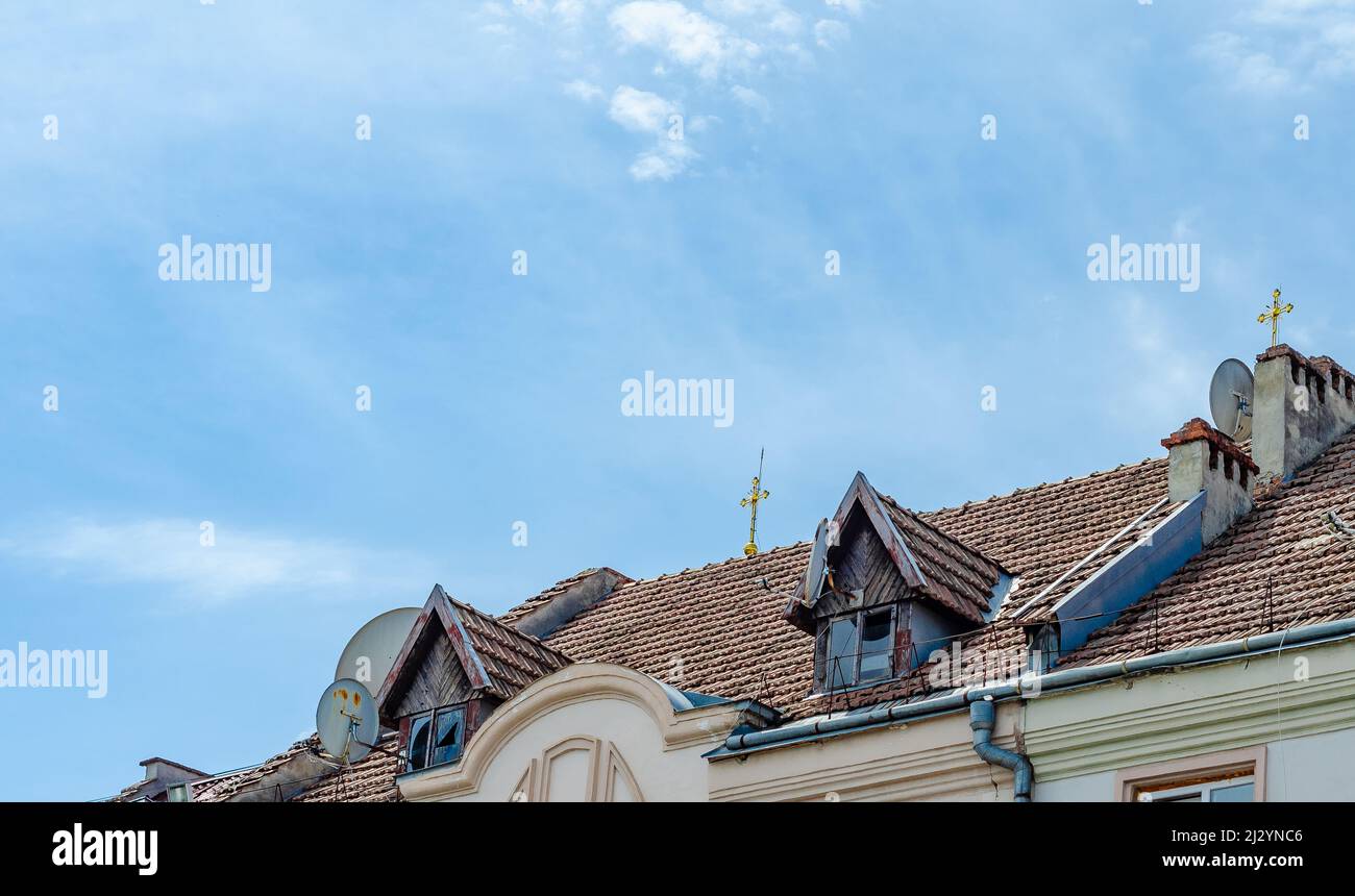Dach des alten Gebäudes. Fliesen, kleine hölzerne Sichtfenster, Steinkamine. Goldene Kreuze auf dem Gebäude. Stockfoto