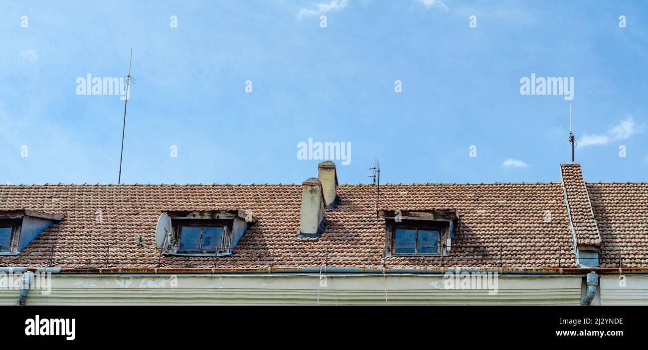 Dach des alten Hauses. Fliesen, kleine hölzerne Sichtfenster, Steinkamine. Stockfoto