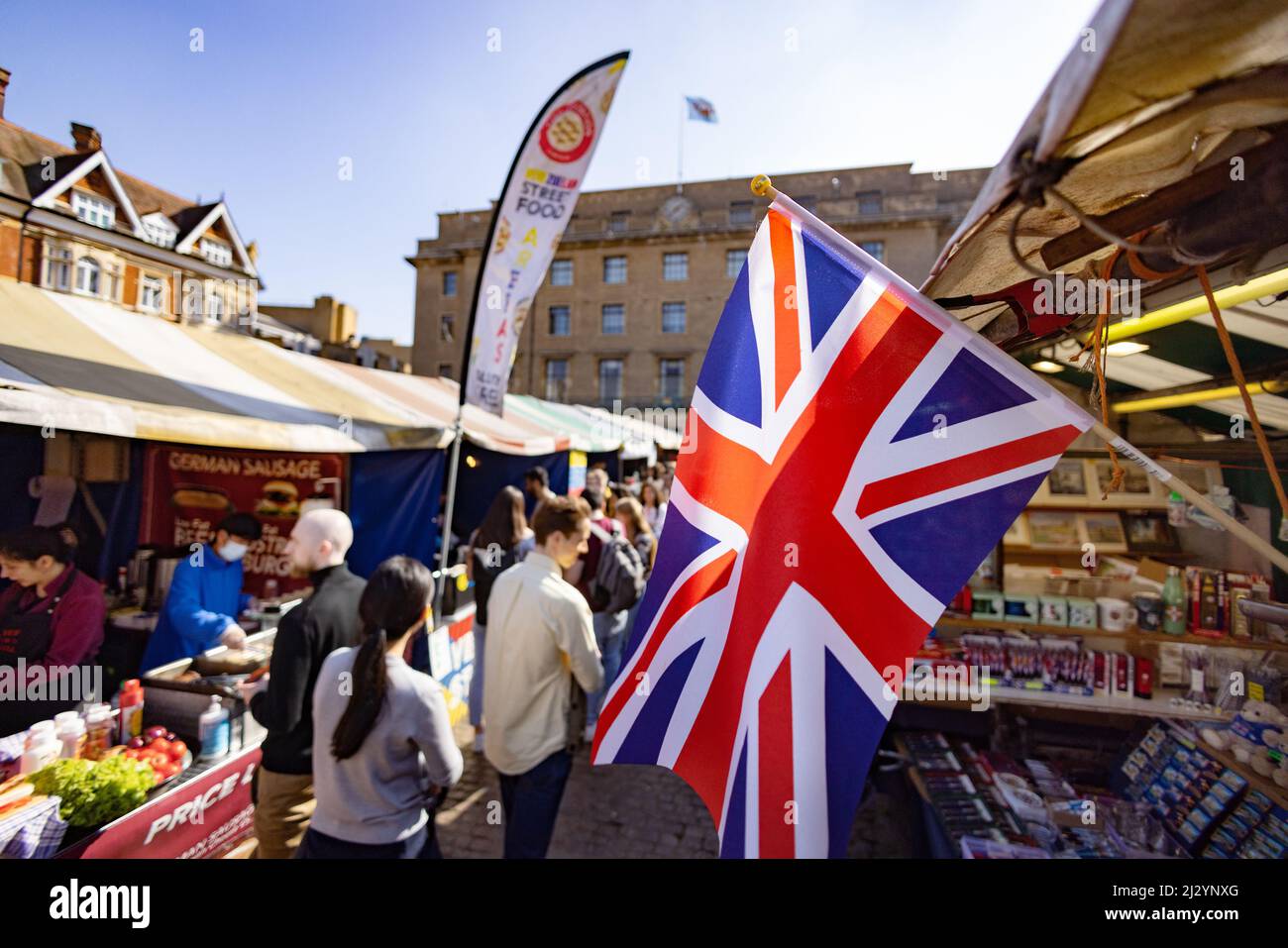 Market UK; Menschen, die an Marktständen einkaufen, und eine Union Jack-Flagge, Cambridge Market, Market Square Cambridge UK Stockfoto