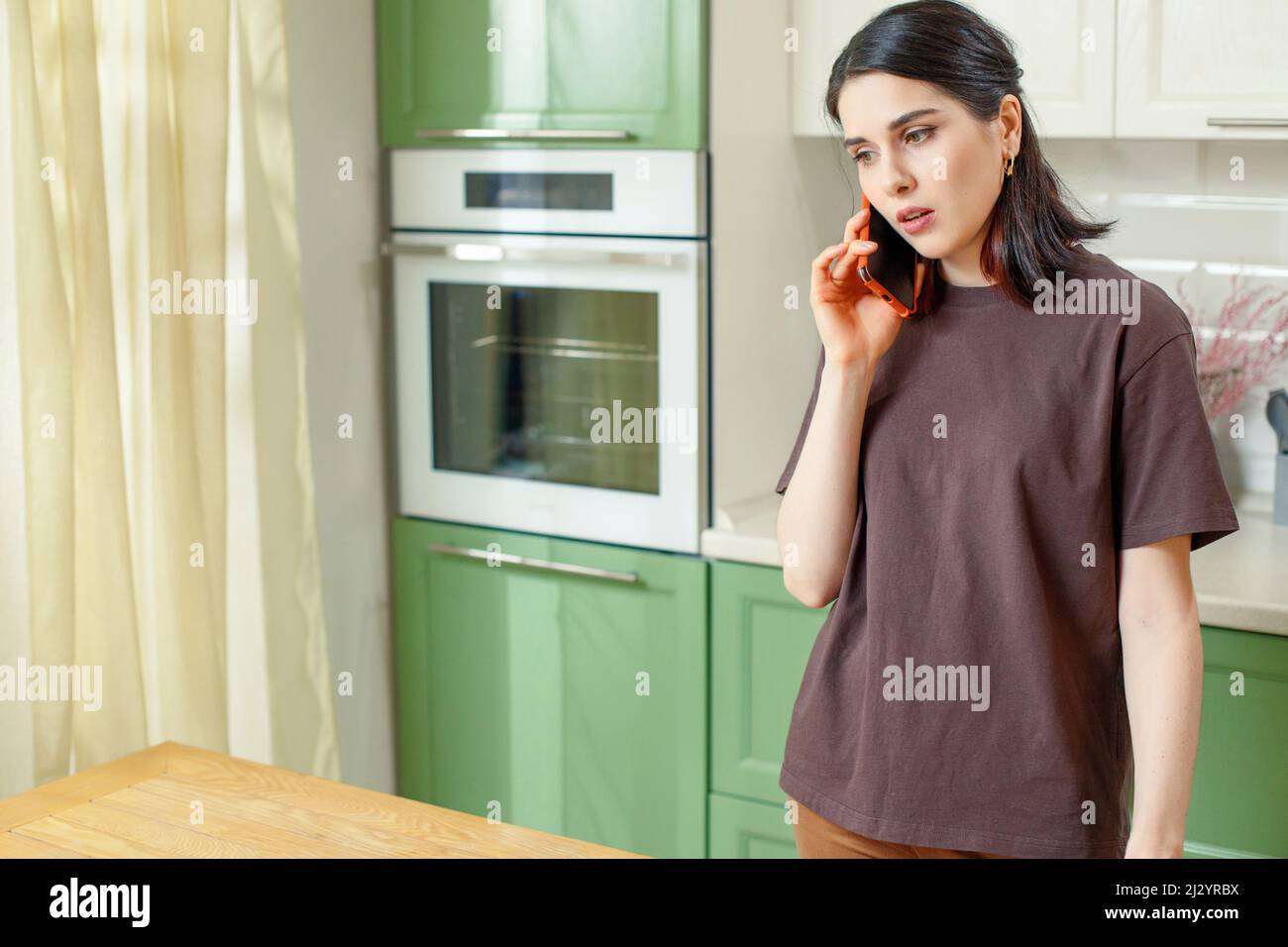 Eine junge Brünette Frau in der Küche spricht auf einem Smartphone. Stockfoto