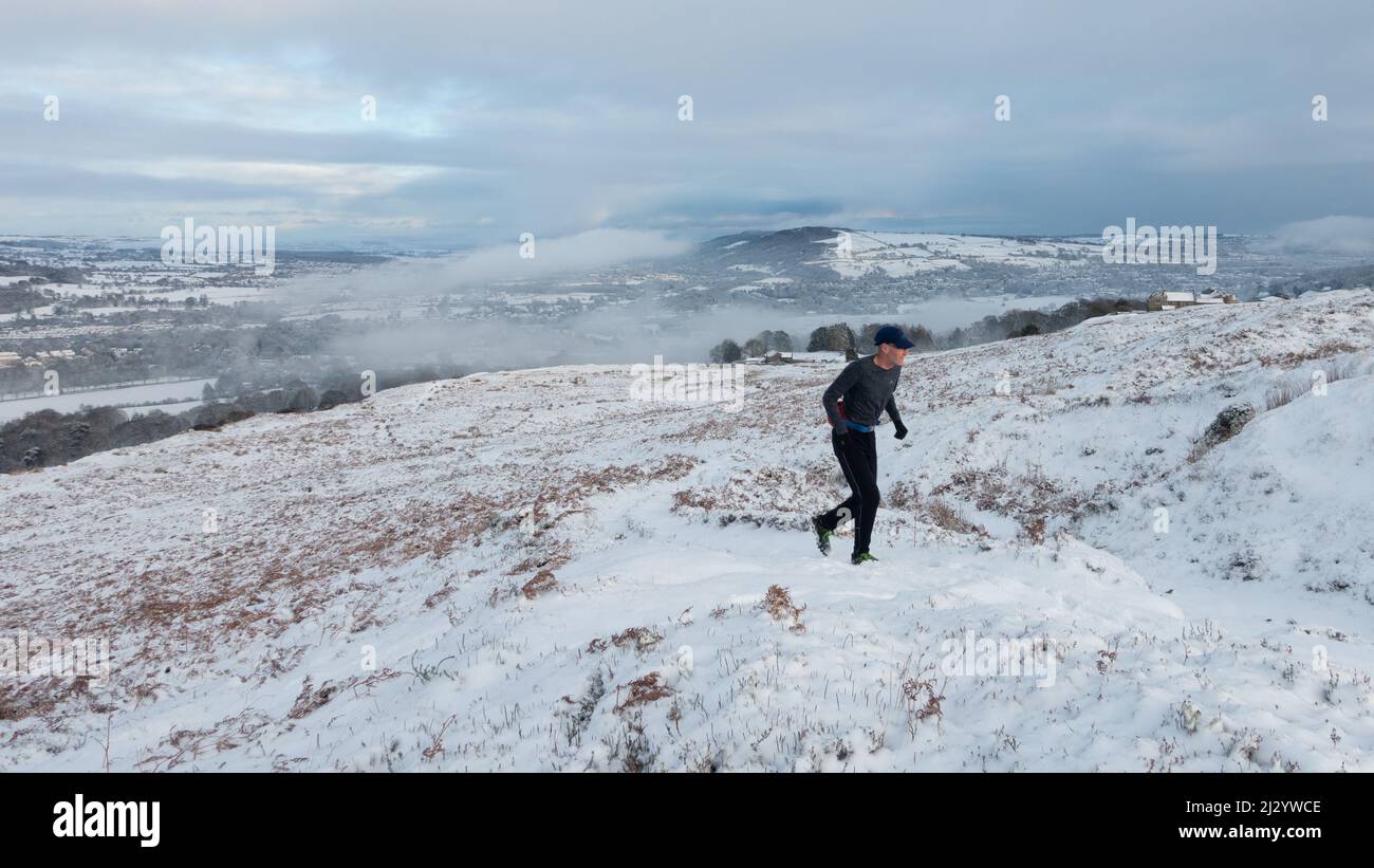 Fell Runner genießt verschneite Moore, während Schnee das Dorf Burley-in-Wharfedale bedeckt und Burley Moor in ein Winterwunderland verwandelt, West Yorkshire, England Stockfoto