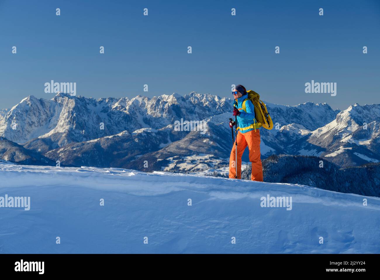 Frau, die mit Schneeschuhen auf ihrem Rucksack über Schneehöhe wandert, im Hintergrund das Kaisergebirge, Hochgern, Chiemgauer Alpen, Oberbayern, Bayern, Deutschland Stockfoto