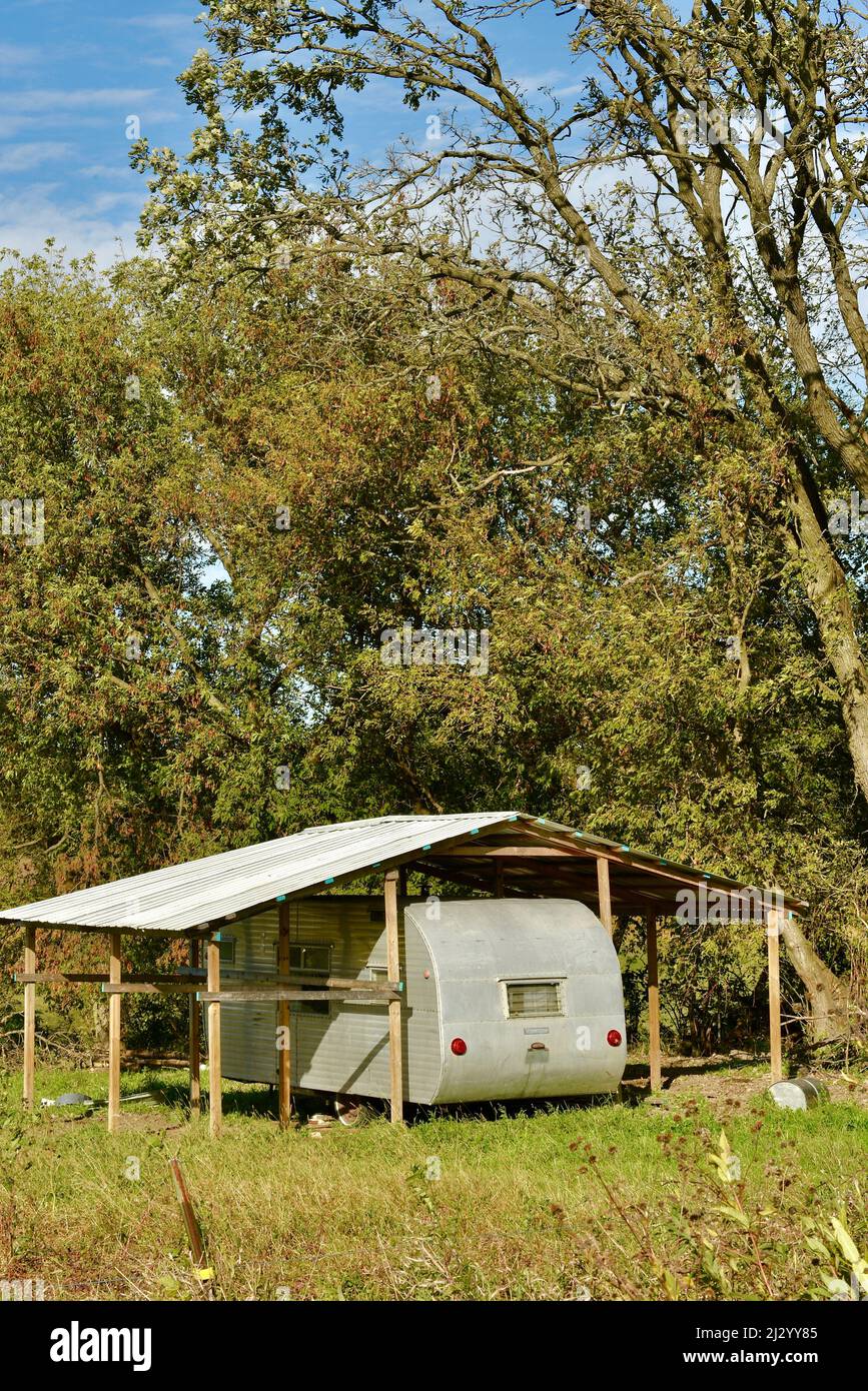 Trendy, hip, Silber Metall vintage Wohnwagen geparkt unter schützendem Metalldach auf abgelegenen Campingplatz auf Farm Hügel unter Bäumen, Osseo, Wisconsin, USA Stockfoto
