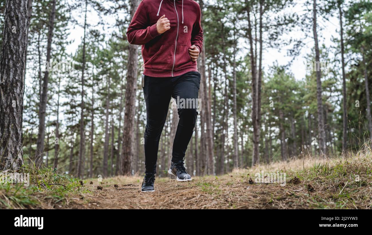 Seitenansicht Körper eines Mannes junger kaukasischer Rüde läuft durch den Wald in der Natur joggen im Herbst oder Frühling Tag - Sport Fitness und recreati Stockfoto