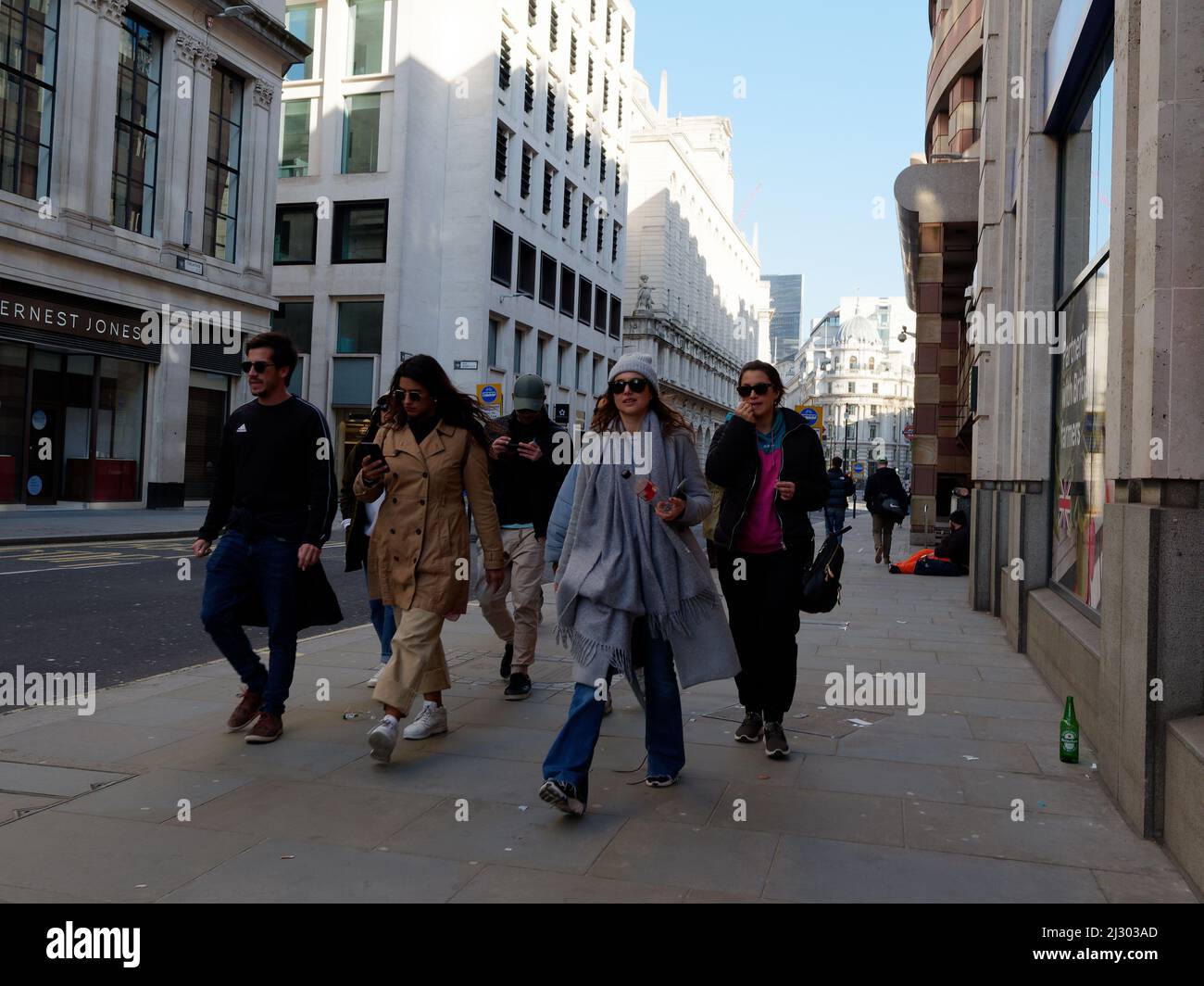 Eine trendige Gruppe junger Freunde geht in der City of London mit Hüten und Sonnenbrillen die Straße entlang. Stockfoto