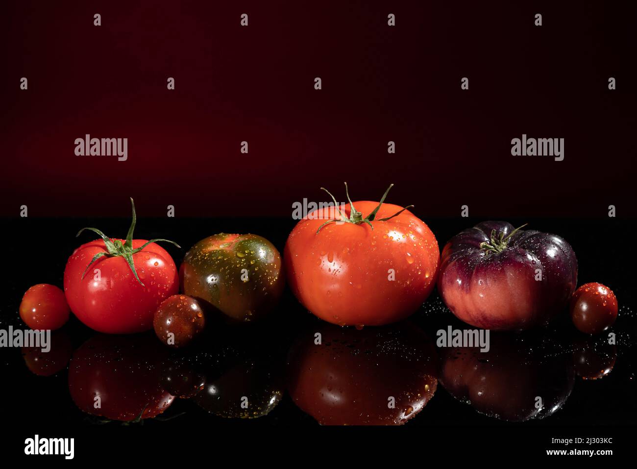 Bunte Tomaten in verschiedenen Größen und Arten auf rot dunklem Hintergrund mit Kopierraum. Stockfoto