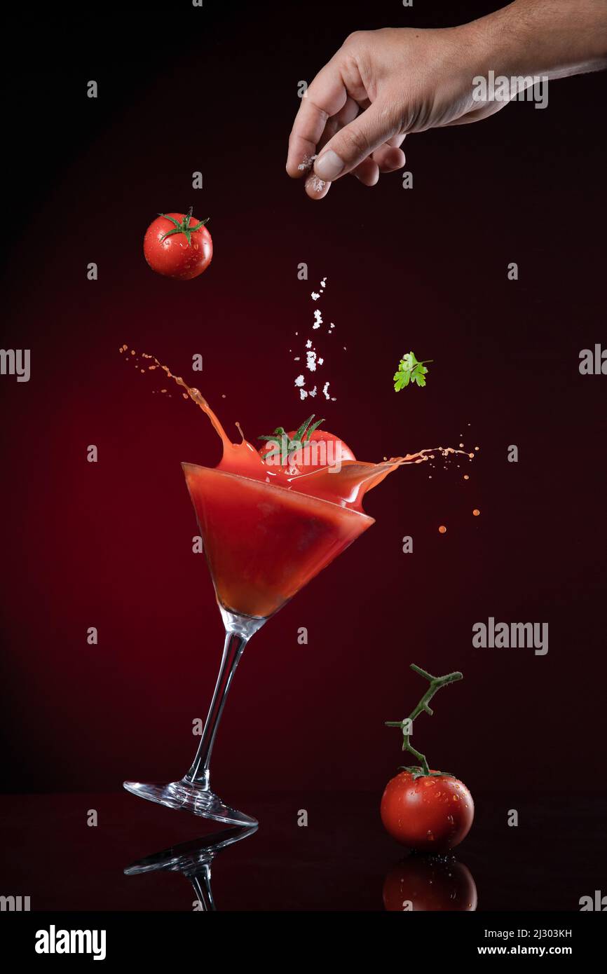Tomate fallen in Tomatensaft mit Explosion und Verspritzung von Tomatensaft auf dunkelrotem Hintergrund. Juice Levitation Konzept. Stockfoto
