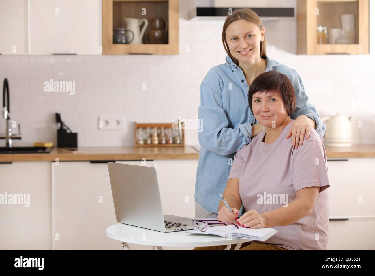 Junge Frau, die ältere Mutter lehrt, das Internet auf dem Laptop zu Hause zu nutzen. Tochter hilft ihrer älteren Mutter, es online mit ihrem persönlichen Konto herauszufinden Stockfoto