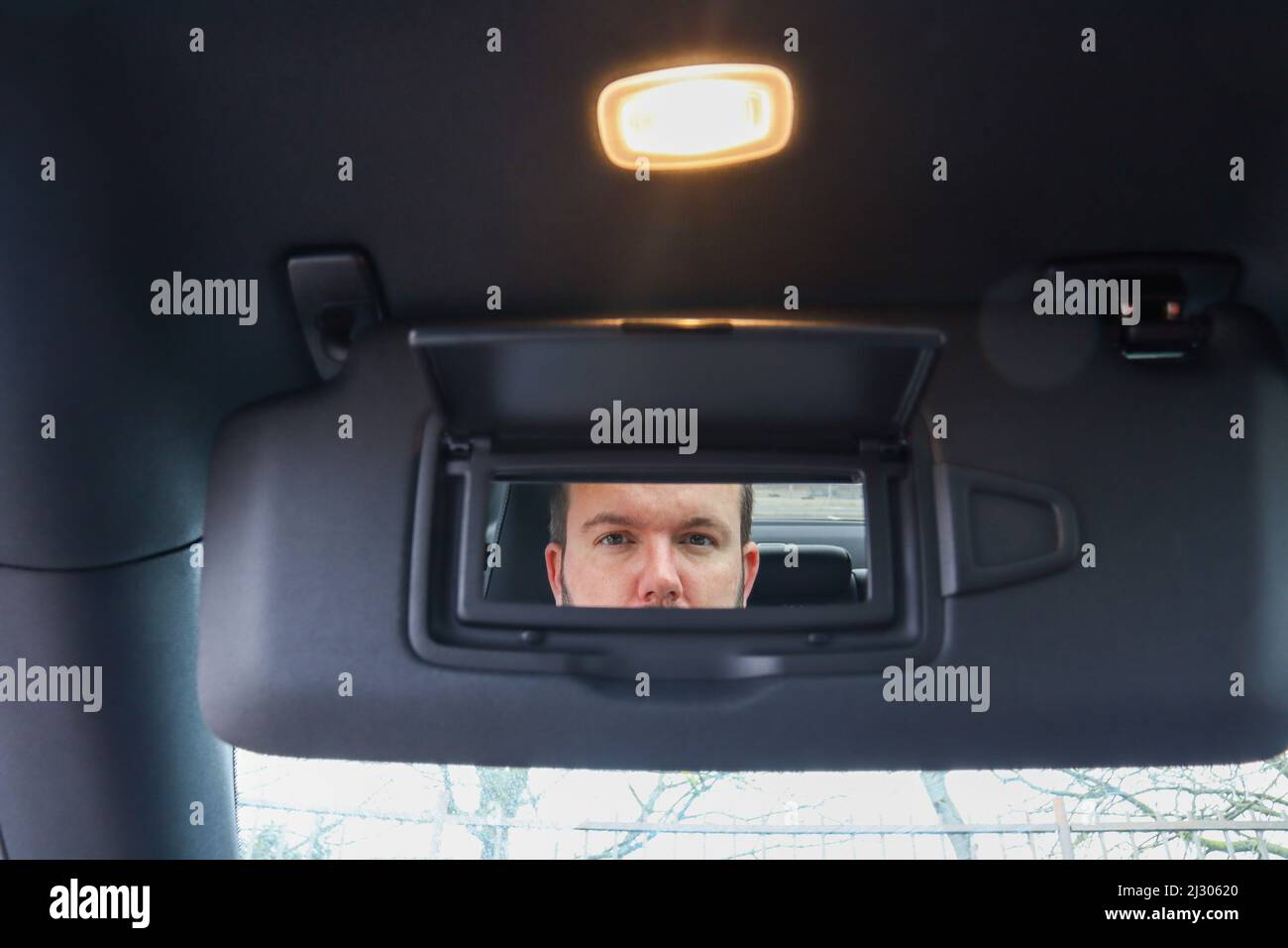 Mann im Spiegel / Mann in einem Kosmetikspiegel auf einem Auto Sonnenblende / Fahrzeug Sonnenschutz Stockfoto