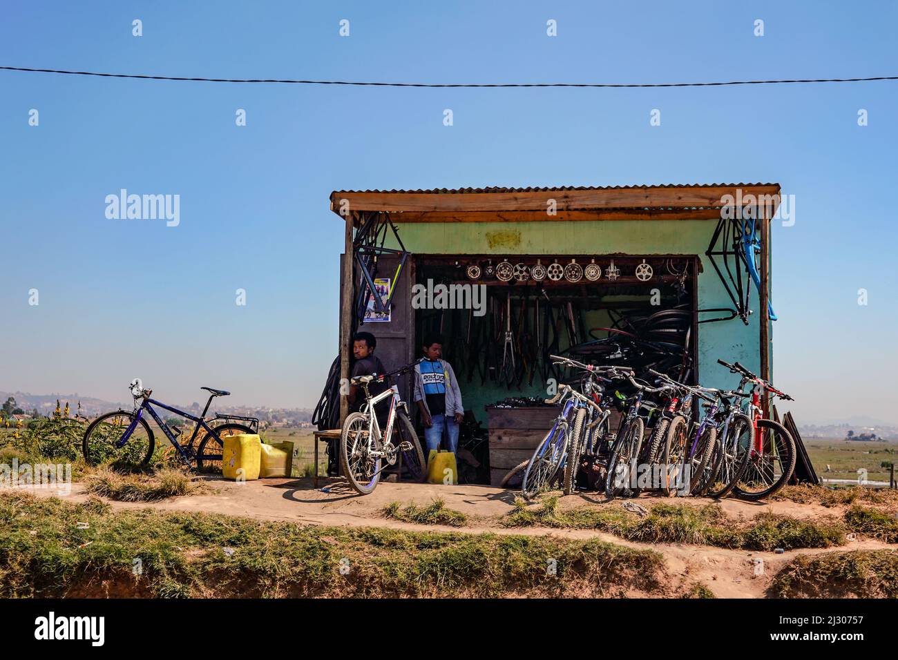 Antananarivo, Madagaskar - 07. Mai 2019: Kleiner provisorischer Barackenladen mit Fahrradteilen und gebrauchten Fahrrädern in der Nähe der Hauptstraße, zwei madagassische Männer in der Nähe Stockfoto