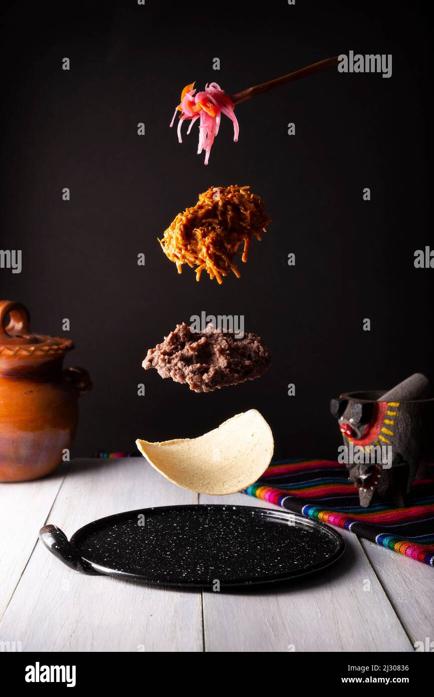 Taco de Cochinita Pibil Levitation. Elemente für die Herstellung eines Taco de Cochinita, Maistortilla, gebackene schwarze Bohnen, Cochinita pibil Eintopf und Zwiebel mit manz Stockfoto