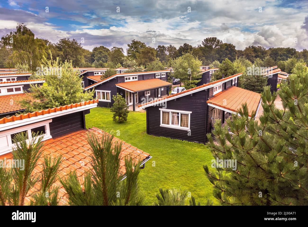 Ferienbungalow Park mit identischen Hütten in symmetrischer Reihenfolge in grüner Waldgegend. Holzchalets mit orangefarbenen Dachziegeln in Gras und Büschen. N Stockfoto