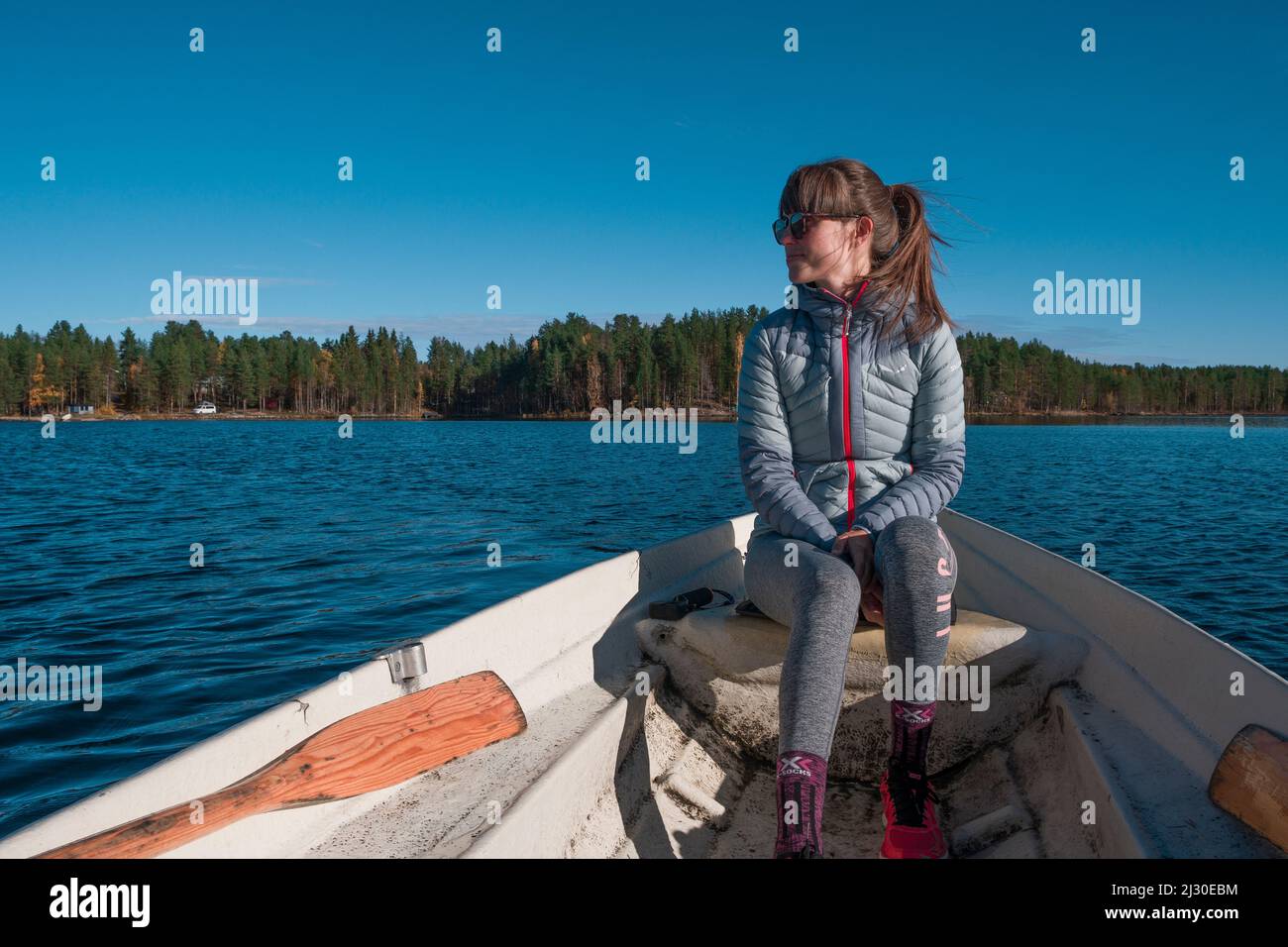 Frau, die im Paddelboot auf dem See in Lappland mit Sonne und blauem Himmel sitzt Stockfoto