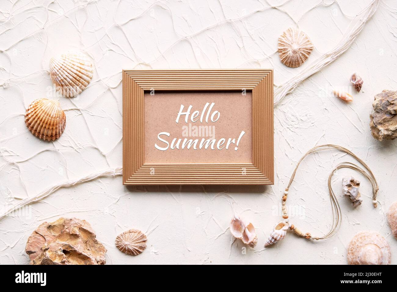 Text Hallo Sommer in goldenem Rahmen. Weißer Hintergrund mit Seesternen, Muscheln, Muscheln, Muscheln, Halskette. Fischernetz auf cremebeige off weißen Hintergrund. Stockfoto